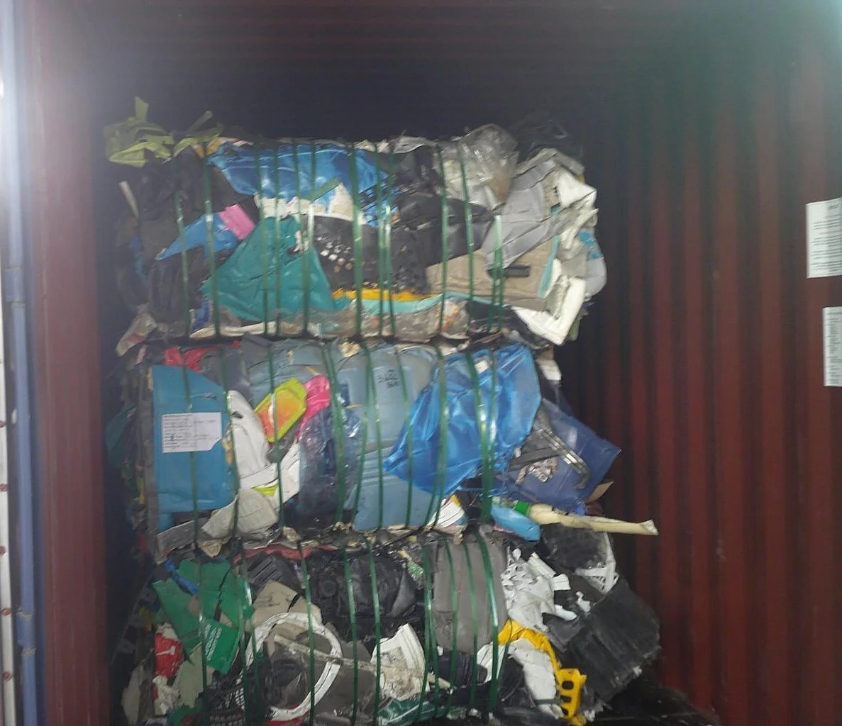 Strapped bales of mixed rigid plastic inside a red shipping container